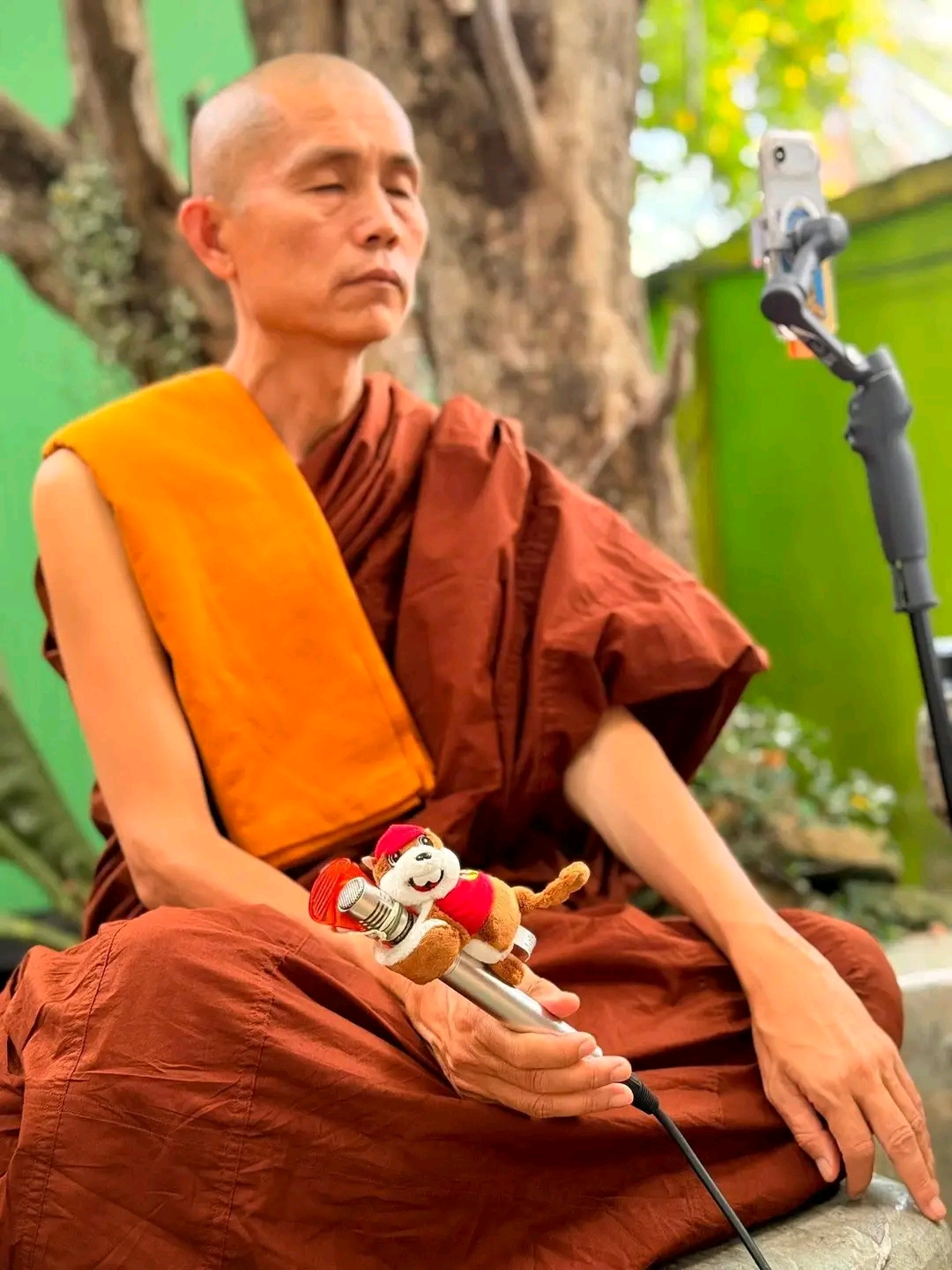 Sayadaw Ashin Ottamathara seated outdoors with a microphone.
